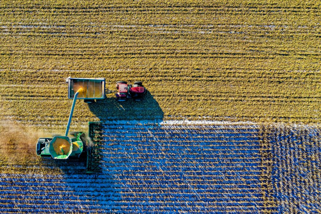 Aerial view of a combine harvester unloading crops into a tractor trailer in a harvested field.