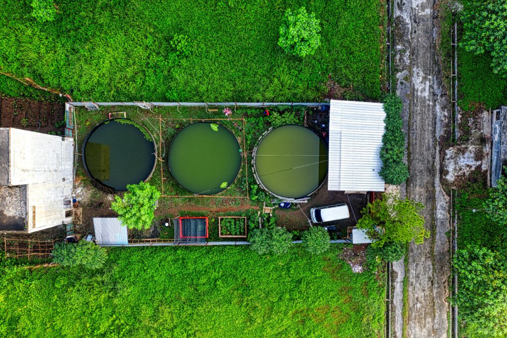 Top view of a green farm setup with circular tanks and plants, selected in a digital interface.